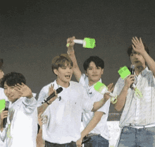 a group of young men are standing in front of microphones holding up green sticks