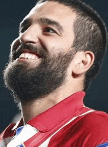 a man with a beard is smiling and wearing a red and blue shirt .