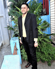 a man wearing a suit and a yellow shirt is standing in front of a blue wall