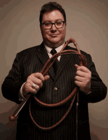 the man is wearing a suit and tie and holding a whip .