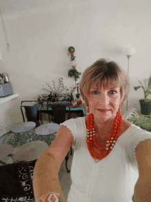 a woman wearing a white shirt and a red necklace takes a selfie in front of a table