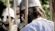 a man wearing a helmet and holding a sword is standing in front of a group of men holding spears .