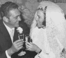 a black and white photo of a bride and groom toasting each other with champagne glasses .