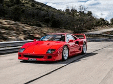 a red ferrari f40 is driving down a road with mountains in the background .