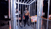 two wrestlers are walking out of a cage at a wrestling event .