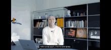 a woman sitting at a desk with a laptop and a bookshelf behind her