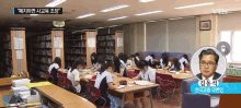 a group of people are sitting at tables in a library with a man in a red tie standing in front of them