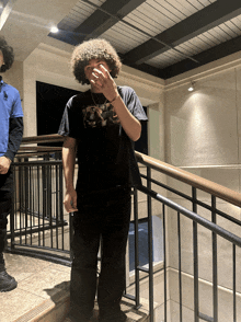 a man with curly hair wearing a black shirt with the letter a on it smoking a cigarette