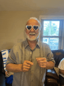 an elderly man wearing heart shaped sunglasses stands in front of a couch