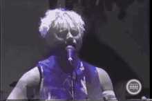 a man with white hair is singing into a microphone while playing a guitar .