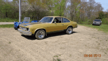 a yellow car is parked in a dirt lot on a sunny day