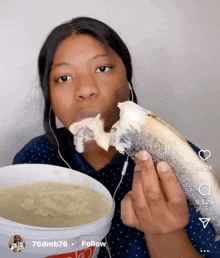 a woman is eating a fish with a bucket of soup in the background