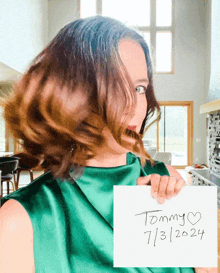 a woman in a green dress is holding a sign that says tommy