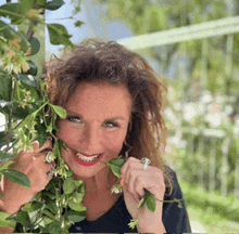 a woman with a ring on her finger is smiling behind a bush with flowers