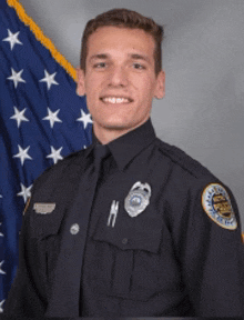 a young man in a police uniform is smiling in front of an american flag