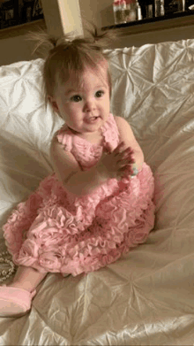 a baby girl is sitting on a bed wearing a pink dress and pink shoes .