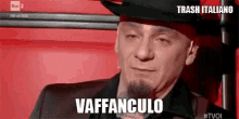 a man with a beard and a hat is sitting in a red chair and says vaffanculo .