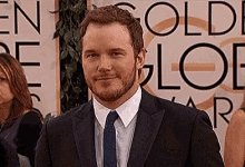 a man in a suit and tie is smiling in front of a sign that says golden globe awards .