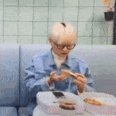 a man wearing glasses is sitting at a table eating pizza