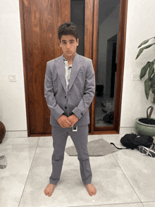 a young man in a suit stands barefoot in front of a wooden door