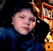 a young boy is sitting in front of a bookshelf looking at the camera .