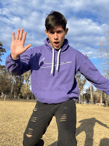 a young man wearing a purple nike hoodie is making a stop sign