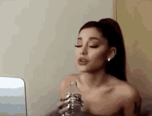 ariana grande is drinking water from a bottle while looking at a laptop .