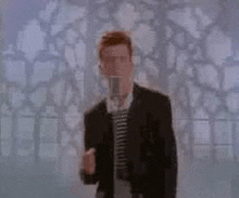 a man in a suit is singing into a microphone in front of a wall .