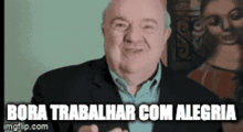 a man in a suit is smiling in front of a painting and the words bora trabalhar com alegria are above him .