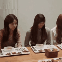 three women are sitting at a table with plates of food on it .