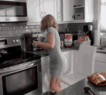 a woman in a grey dress is standing in a kitchen preparing food with a bag of whole flour on the counter