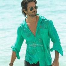 a man wearing a green shirt and sunglasses is walking out of the water .