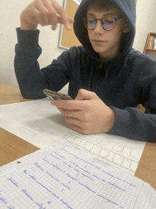 a boy wearing glasses and a hoodie is looking at his cell phone