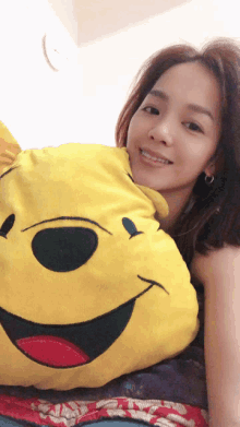 a woman is holding a yellow pillow with a winnie pooh face on it