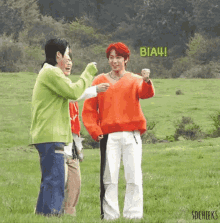 a group of young men are standing in a grassy field . one of the men is wearing an orange sweater .