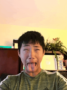 a young man making a funny face with his tongue out wearing a green adidas shirt