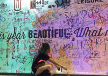 a woman squats in front of a wall that has graffiti on it including the words " is year beautiful what "