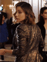 a woman wearing a black and gold jacket stands in a crowd of people