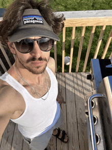 a man wearing sunglasses and a patagonia hat stands on a deck