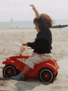 a little girl sits on a red bobby car