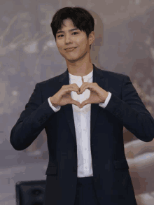 a man in a suit and white shirt making a heart shape with his hands