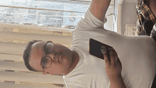 a man wearing glasses and a white shirt is holding a black cell phone