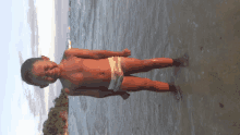 a young boy in swim trunks stands on the beach