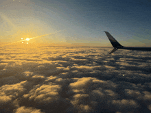 the wing of an airplane flying over the clouds at sunset