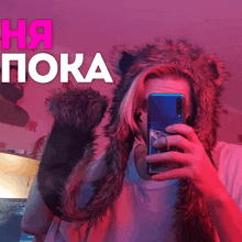 a person wearing a furry hat taking a selfie in front of a sign that says ha poka