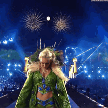 a woman in a green dress is walking in front of fireworks
