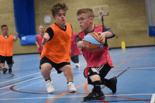 a young boy dribbles a basketball while another boy watches