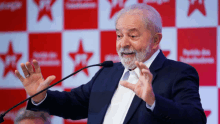 a man in a suit and tie is speaking into a microphone in front of a red star backdrop