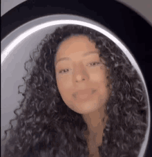 a young woman with curly hair is taking a selfie in front of a mirror .