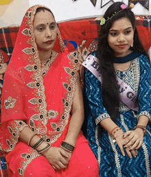 a woman wearing a sash that says baby girl sits next to a woman in a blue dress